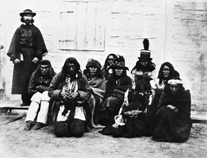 Picture of Jean L’Heureux in a cassock with a group of Blackfoot, Blood and Peigan Indians